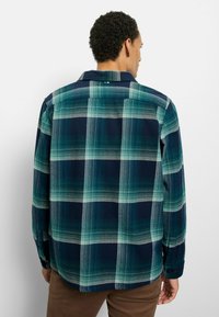 Flanellhemd in dunklem Navy mit grünem und hellblauem Karomuster. Lange Ärmel, Kragen und Knopfmanschetten. Weiche Textur.