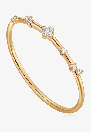 Goldfarbener Armreif-Ring mit einem schlanken, dünnen Design und fünf verstreuten, runden Diamanten unterschiedlicher Größen entlang des Rings.