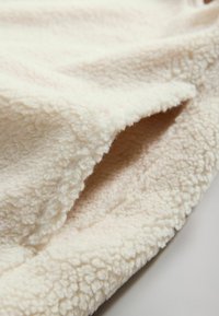 Krämfärgad fleecefilt med en mjuk, texturerad yta, som har en något plyschig känsla och rundade kanter.