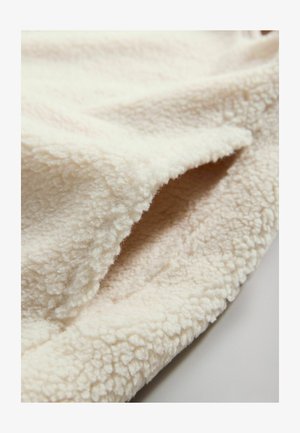 Krémově zbarvená fleecová deka s měkkým, texturovaným povrchem, která má mírně plyšový pocit a zaoblené okraje.