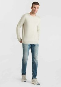 Licht beige lange-sleeve sweater, zachte textuur, gecombineerd met middenblauwe vervaagde jeans. Draag met grijze sport sneakers, staand tegen een effen achtergrond.