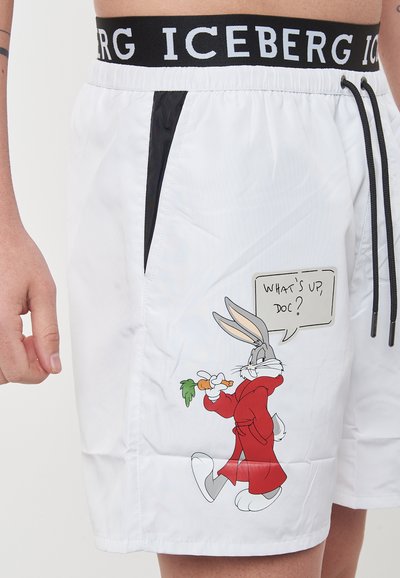 Pantaloni da bagno bianchi con un elastico in vita nero con logo, tasche laterali e una grafica stampata di Bugs Bunny che tiene una carota, con un fumetto.