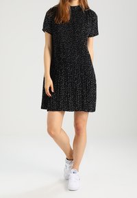 Vestido negro de manga corta con falda acampanada, con manchas blancas por todo su tejido. Combinado con zapatillas blancas. Textura de tela suave.