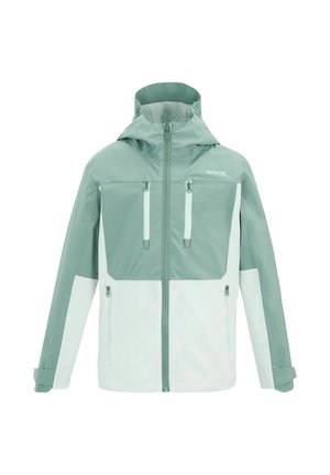 Fille portant une veste bleu sarcelle et blanche, un t-shirt bleu sarcelle avec un motif de montagne, un short foncé, des chaussures de randonnée, tenant un sac à dos vert par une bretelle.