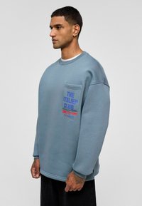 Overmaatse blauwe sweatshirt van katoen, met een borstzak en grafische tekst in rood en blauw. Soepele textuur met geribbelde manchetten.