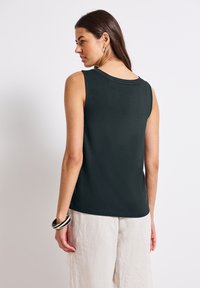 Bezrukávový tmavě zelený top z hladké látky s kulatým výstřihem, doplněný světle barevnými, volně střiženými lněnými kalhotami.