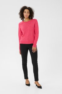 Pull en maille rose avec un col rond, des manches longues et des poignets côtelés. Associé à un jean noir slim et des escarpins noirs à lanières.