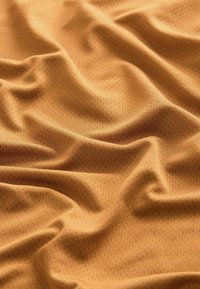 Materiał w kolorze miodowym o fakturze z małymi, wypukłymi kropkami. Tkanina wydaje się miękka i gładko się układa.