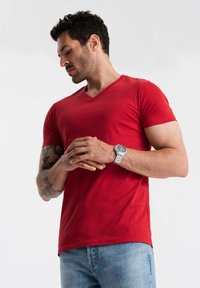 Rød V-hals t-shirt lavet af blødt stof, tætsiddende design, korte ærmer, parret med lyseblå jeans og et sølvur på håndleddet.