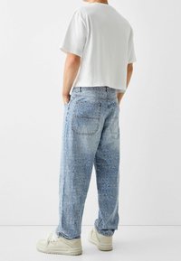 Lösa ljusblå denimjeans med präglat textmönster, i kombination med en kortärmad vit t-shirt och off-white sneakers.