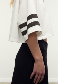 Witte cropped t-shirt met zwart-witte gestreepte mouwen, met een ontspannen pasvorm. Gecombineerd met een zwarte strakke onderkant.