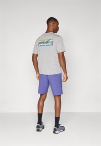 Gray short-sleeve T-shirt with a colorful Patagonia logo on the back, paired with purple shorts and black socks, worn with gray athletic shoes.