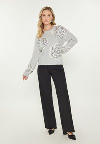 Maglione grigio lavorato a maglia con grandi motivi di rose in paillettes, abbinato a pantaloni larghi neri e scarpe con tacco nere.