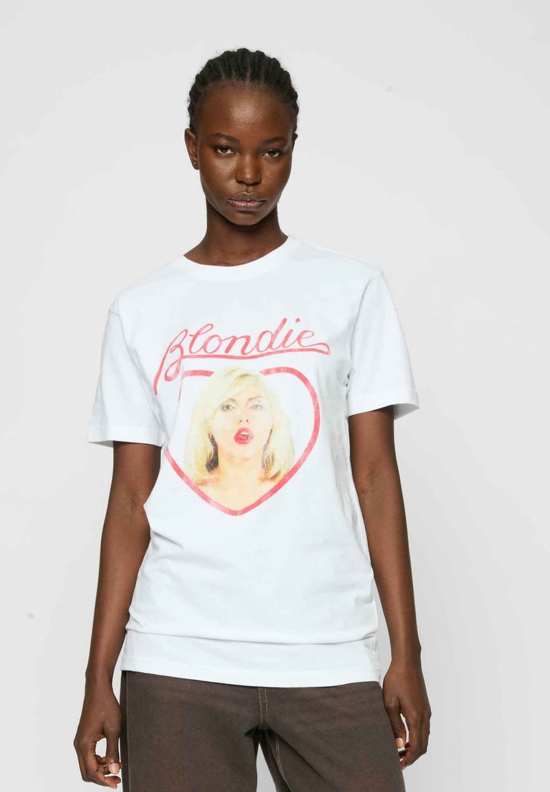 T-shirt en coton blanc avec un graphique coloré représentant une femme blonde à l'intérieur d'un cœur rouge, avec le texte "Blondie" en rose au-dessus de l'image.
