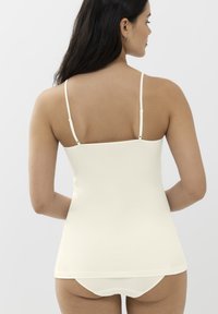 Camisola elasticizzata color crema con sottili spalline regolabili, caratterizzata da una texture liscia e un design aderente, che arriva fino all'anca.