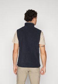 Navy fleece vest with high collar, sleeveless design, and no visible fastenings. The inner layer is soft, and it has a relaxed fit.