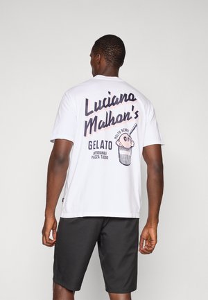 Hvit bomull T-skjorte med stor svart tekst som sier "Luciano Malhan's" og en illustrert iskremkjeks på baksiden. Kombinert med svarte shorts.