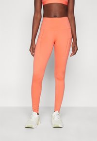 Klare oransje leggings laget av stretchy materiale med høy midje, med to frontlommer og en glatt, matt tekstur.