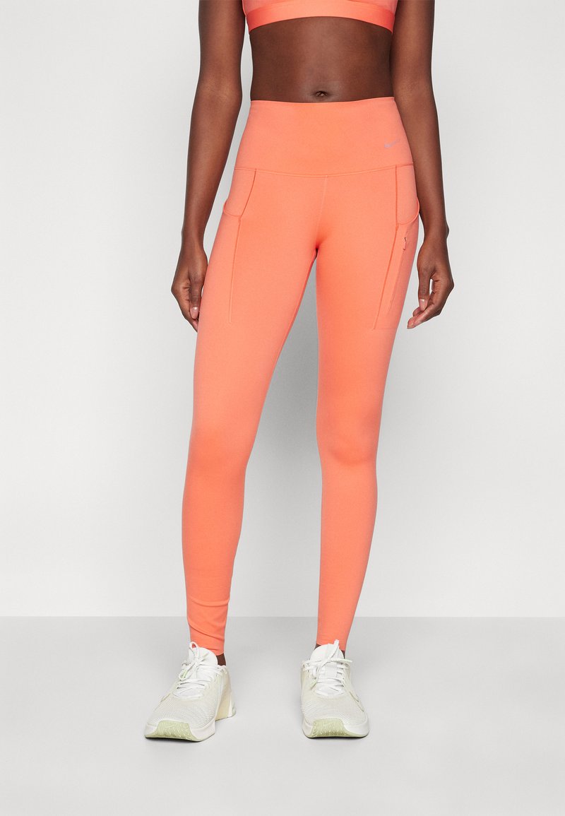 Klare oransje leggings laget av stretchy materiale med høy midje, med to frontlommer og en glatt, matt tekstur.