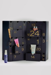 Calendario dell'Avvento con sfondo blu scuro, numeri dorati e molteplici scomparti. Contiene vari prodotti di bellezza, tra cui creme e sieri.