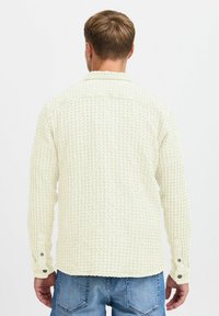 Camisa de botones color beige claro con un patrón de punto waffle texturizado, bolsillo en el pecho y puños abotonados. Corte casual con una sensación suave.