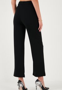 Black wide-leg trousers made of smooth fabric, featuring a sleek design and a mid-rise waist. Paired with black and white snake print heels.