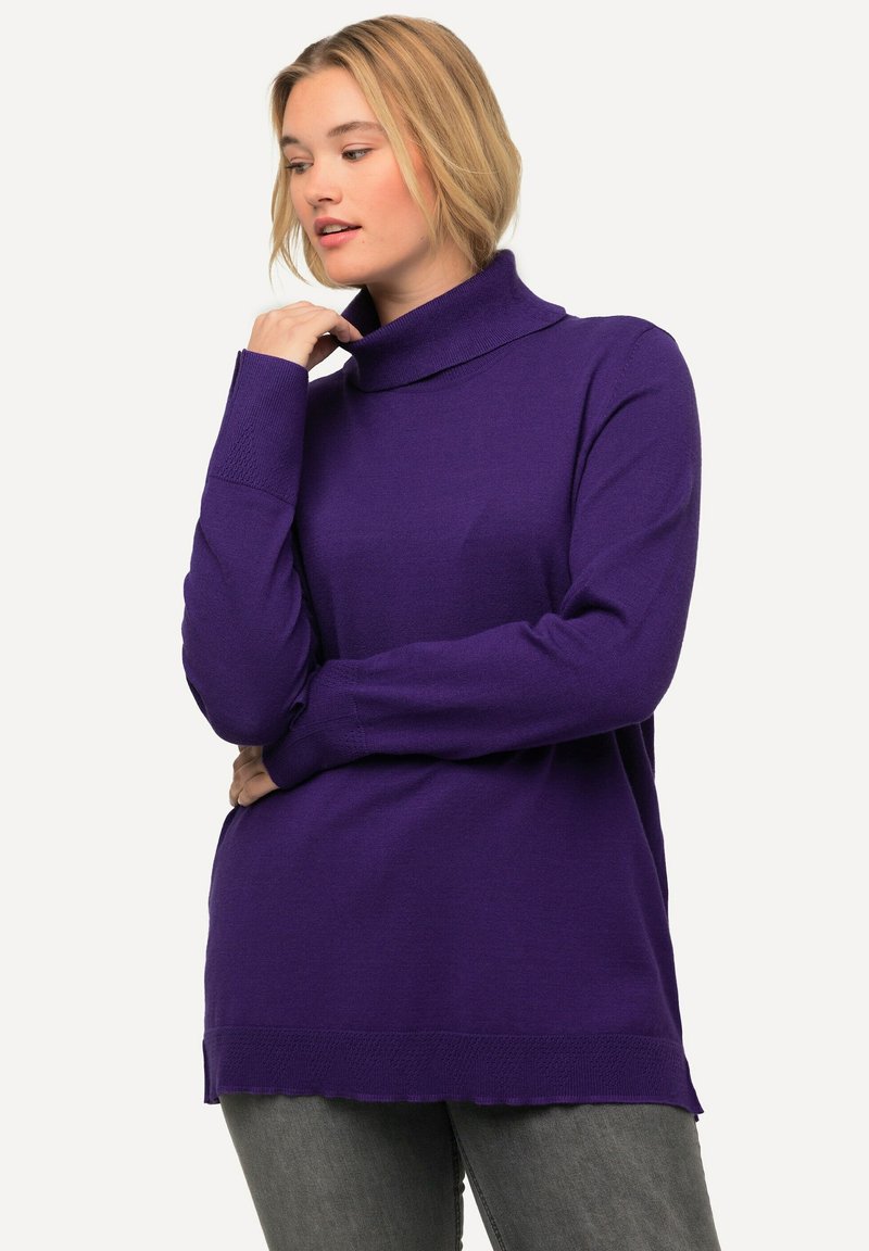 Maglione a maniche lunghe con collo a dolce vita di un vivido viola, caratterizzato da un design a costine, fessure laterali e una texture morbida, abbinato a jeans grigi scuri.