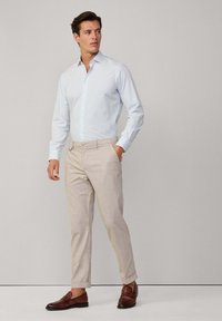 Chemise rayée bleu clair, manches longues, col boutonné ; pantalon beige avec les poignets retroussés ; mocassins marron ; texture lisse sur l'ensemble.