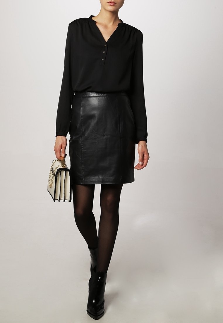 Czarna bluzka z długim rękawem i listwą na guziki, zestawiona z czarną skórzaną ołówkową spódnicą. Modelka trzyma białą i czarną usztywnianą torebkę.