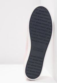 Rosa sneaker med en svart gummisula som har ett präglat mönster av "TOMMY JEANS", vit mellansula och en slät textilöverdel.