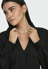 Blusa nera a maniche lunghe con maniche a sbuffo e scollatura a V. Accessoriata con una collana in catena dorata e orecchini a cerchio. Texture liscia.