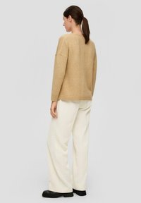 Beige Pullover mit lockerer Passform und überschnittenen Schultern, kombiniert mit cremefarbenen, weit geschnittenen Hosen und schwarzen Plateau-Schuhen. Schlichte, strukturierte Stoffqualität.