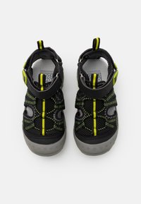 Zapatos de malla negros con suelas grises, acentos en amarillo y verde, con punta cerrada, correas ajustables y un diseño estampado.