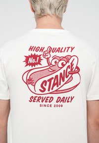 White t-shirt featuring a red graphic of a hot dog with cartoon eyes, text "HIGH QUALITY No.1 STANCE SERVED DAILY SINCE 2009."