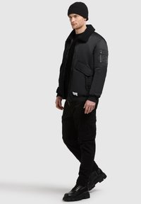 Sort bomberjakke med pelsforet krave, lynlåslomme på armen og oversized pasform. Sammen med sorte cargo-bukser og støvler.