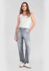 Pantalones de mezclilla gris con un corte relajado, que presentan bolsillos frontales y un ligero desgaste. Combinados con una camiseta sin mangas blanca y zapatillas blancas.
