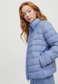 Giacca puffer blu chiaro con collo alto, caratterizzata da pannelli a motivo trapuntato orizzontale e zip frontale. Tessuto morbido e liscio, con tasche laterali.