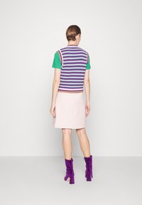 Gilet en tricot à rayures horizontales multicolores sur une chemise verte, associé à une jupe rose pâle et des bottines en daim violet.