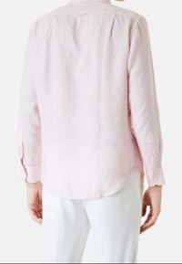 Růžová lněná košile s dlouhými rukávy, knoflíkovými manžetami, kulatým lemem a detailem na zadní části. Stylizováno s bílými kalhotami.