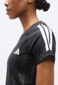 T-shirt de sport noir avec un col en V, des manches courtes et des bandes blanches sur les épaules. Confectionné dans un tissu lisse qui évacue l'humidité.