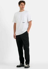 Witte katoenen t-shirt met korte mouwen, ronde hals en bedrukt logo. Gecombineerd met zwarte broek en zwarte schoenen met witte accenten.