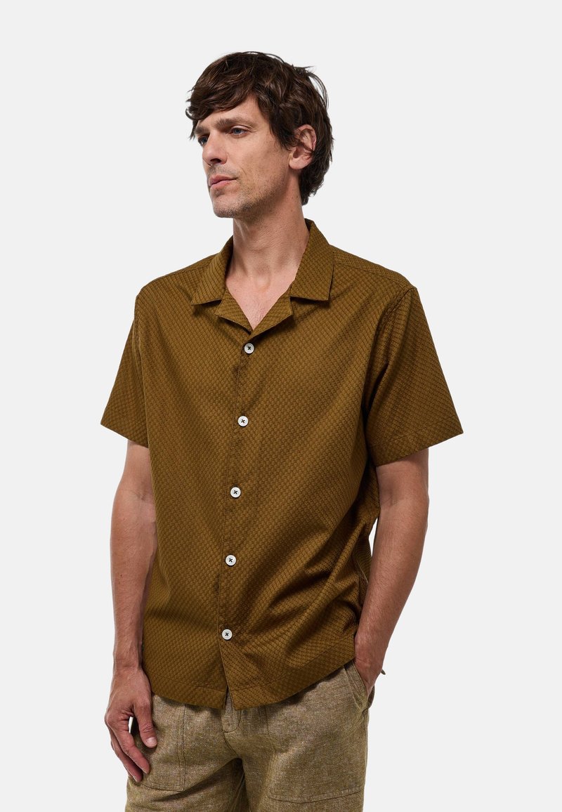 Chemise à manches courtes, à motif marron avec un col boutonné et des boutons blancs, fabriquée en tissu léger avec une finition texturée.