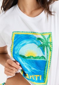 White cotton t-shirt featuring a colorful design of waves, a sun, and palm trees, framed with yellow and green accents.
