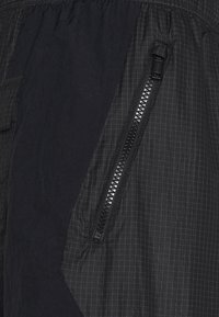 Svart lättviktsmaterial med ett rutmönster, med en ficka med dragkedja och ett rynkat midjeband, som framhäver en stilren design.