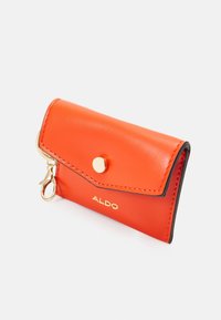 Orange leather card holder with a flap closure, gold hardware, and embossed branding. Features a keychain attachment and contrasting edges.