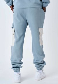 Pantaloni cargo in felpa blu chiaro con polsini a coste, tasche laterali e tasche a soffietto beige in contrasto. Il tessuto ha un aspetto texturizzato.