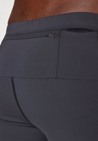 Czarne spodenki sportowe wykonane z elastycznej tkaniny charakteryzują się bezszwowym designem, tylną kieszonką na zamek oraz kontrastującymi detalami w stichach.