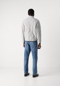 Gray quilted jacket with rounded diamond patterns, high collar, and long sleeves. Worn with blue jeans and black shoes.