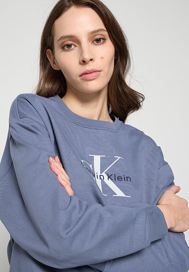 Felpa blu con colletto tondo, adornata da un logo bianco "Calvin Klein". Texture liscia e maniche lunghe con polsini a coste.