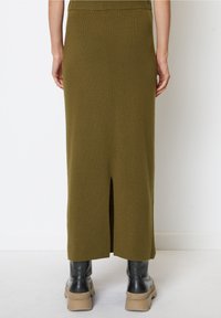 Gebreide olijfgroene rok met een split aan de achterkant. Vloerlange, aansluitende pasvorm, zachte textuur. Gecombineerd met zwarte enkellaarsjes en plateauzolen.